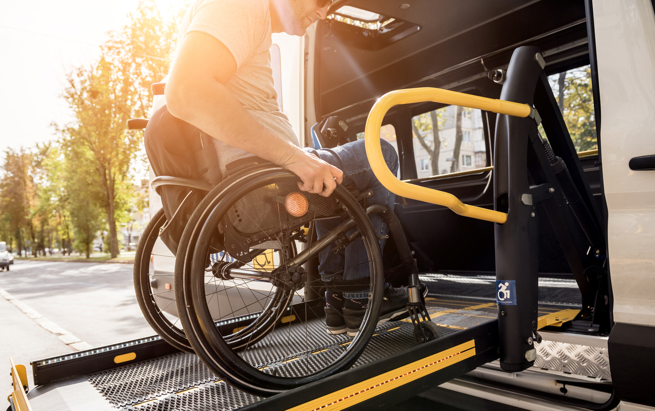 A man in a wheelchair on a lift of a vehicle for people with disabilities.
